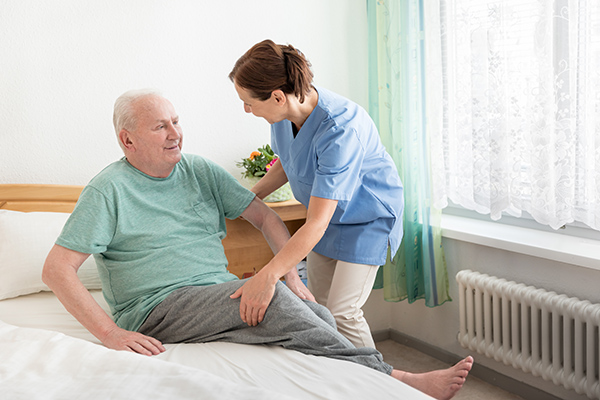 Caregiver assisting senior man out of bed